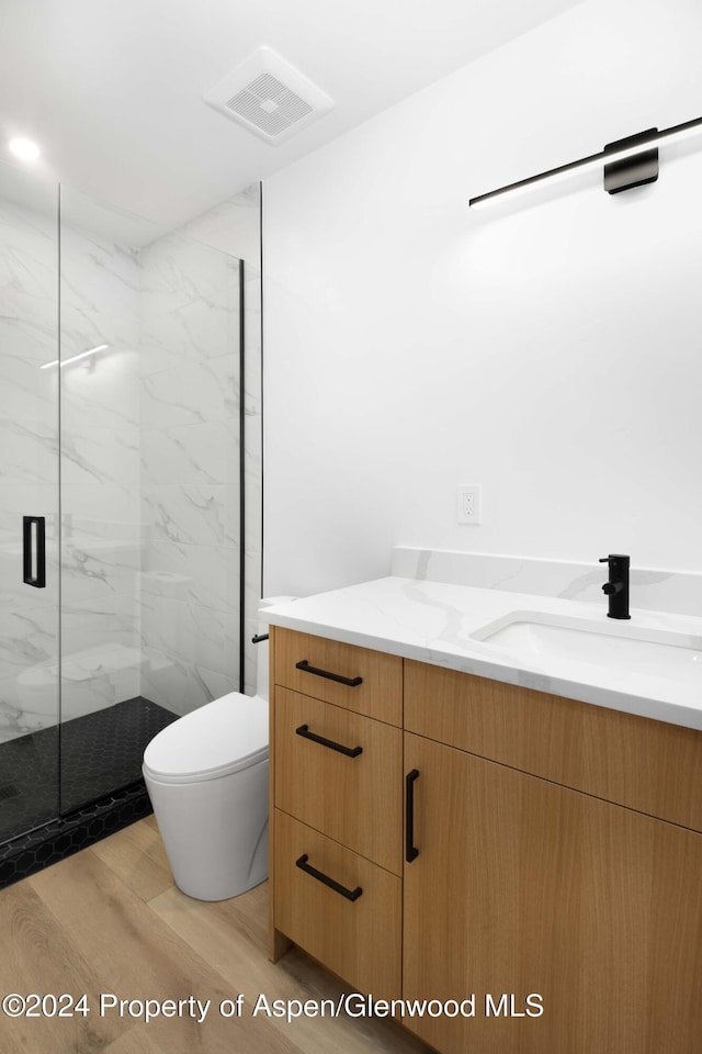 bathroom with hardwood / wood-style floors, vanity, toilet, and a shower with shower door