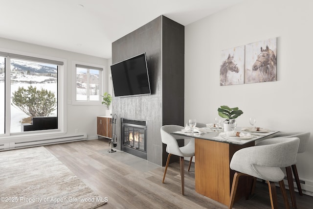 dining area featuring a baseboard heating unit, light hardwood / wood-style floors, and a large fireplace