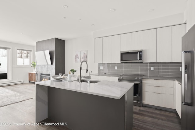 kitchen with appliances with stainless steel finishes, an island with sink, sink, white cabinets, and backsplash