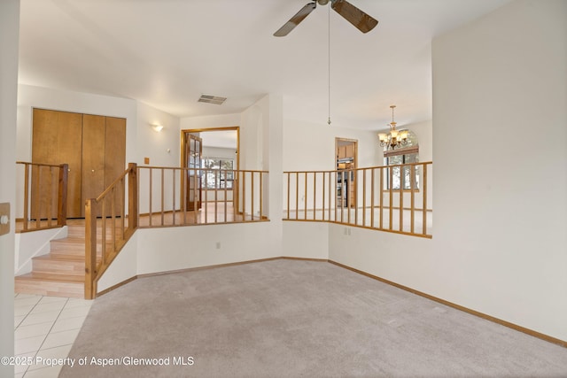 carpeted empty room featuring ceiling fan with notable chandelier