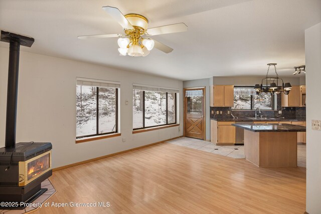 kitchen featuring light brown cabinets, a wood stove, dishwasher, pendant lighting, and decorative backsplash