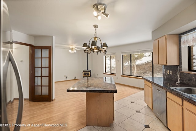 kitchen with appliances with stainless steel finishes, tasteful backsplash, a kitchen island, light brown cabinetry, and a wood stove