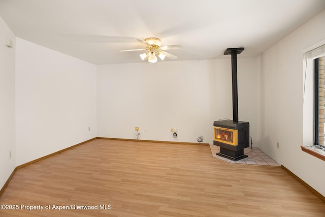 unfurnished living room with ceiling fan, light wood-type flooring, and a wood stove