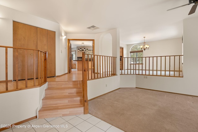 stairs featuring ceiling fan with notable chandelier and carpet