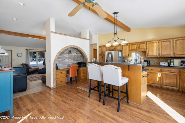 kitchen with stainless steel fridge with ice dispenser, backsplash, pendant lighting, a kitchen bar, and light wood-type flooring