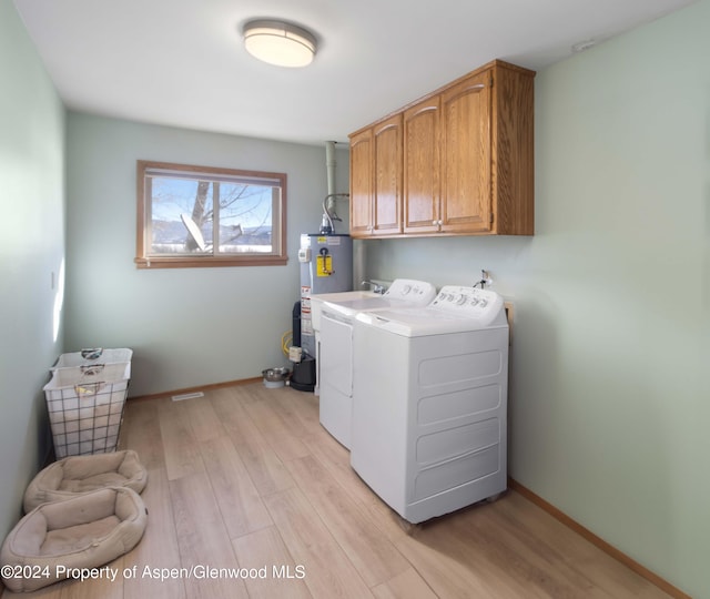 laundry area featuring water heater, washer and clothes dryer, cabinets, and light hardwood / wood-style flooring