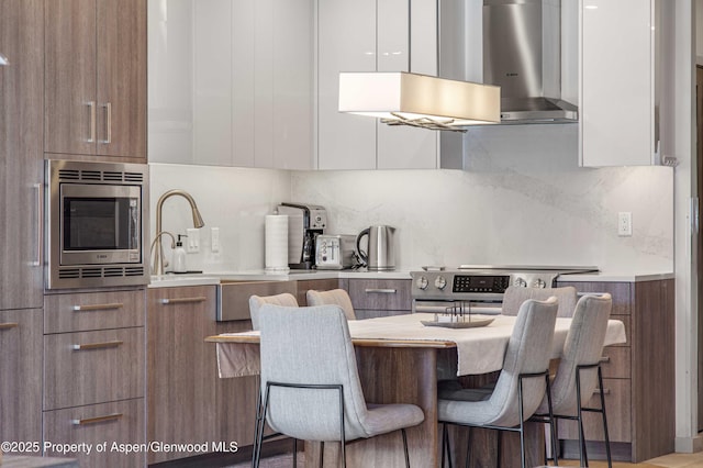 kitchen featuring white cabinetry, exhaust hood, appliances with stainless steel finishes, a kitchen breakfast bar, and decorative backsplash