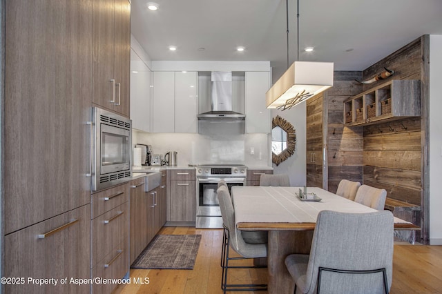 kitchen featuring wall chimney range hood, a kitchen island, stainless steel appliances, white cabinets, and a kitchen bar