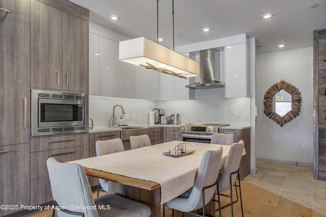 kitchen featuring sink, decorative light fixtures, white cabinets, stainless steel appliances, and wall chimney range hood