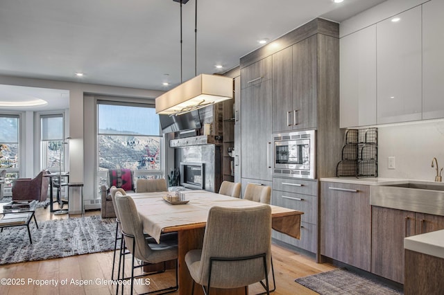 kitchen with stainless steel microwave, sink, light wood-type flooring, and a fireplace