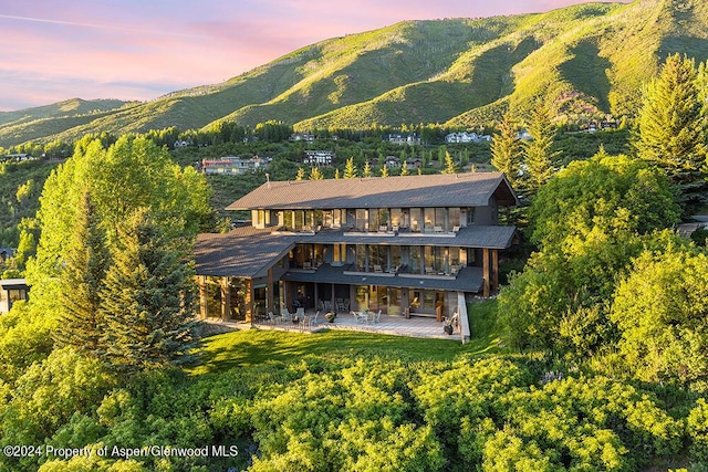 back house at dusk with a mountain view, a balcony, and a patio