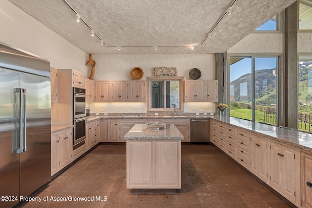 kitchen featuring appliances with stainless steel finishes, light stone counters, sink, a mountain view, and a center island