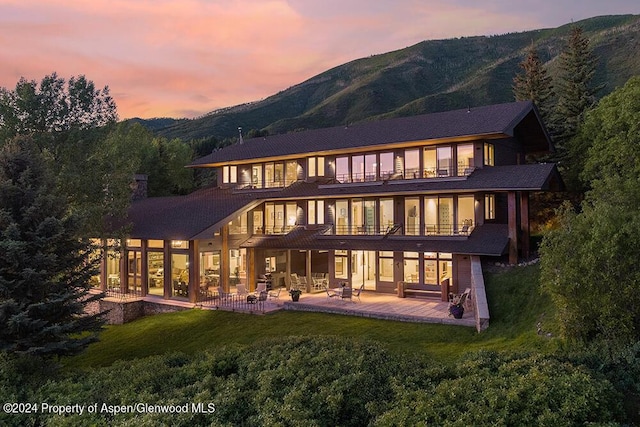 back house at dusk featuring a lawn, a mountain view, a balcony, and a patio