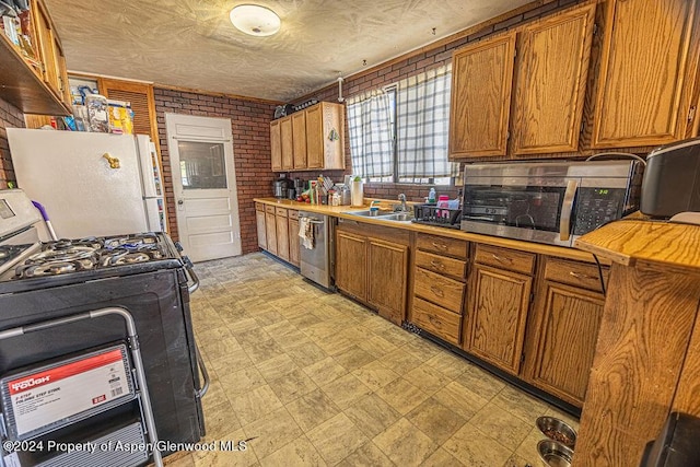 kitchen featuring gas stove, sink, stainless steel dishwasher, brick wall, and white refrigerator