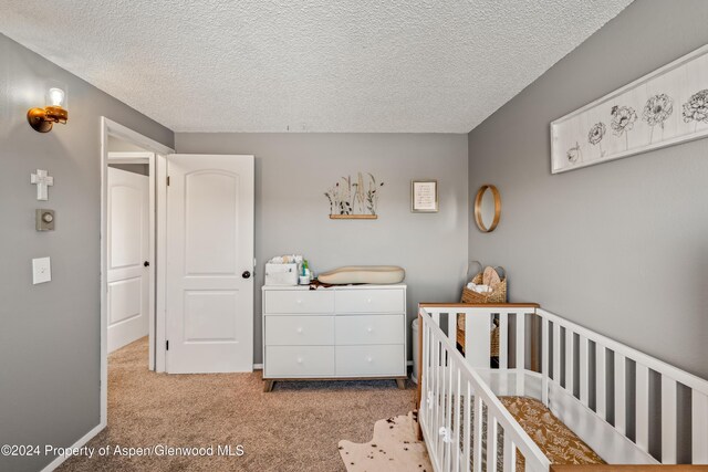 bedroom with light carpet, a textured ceiling, and a crib