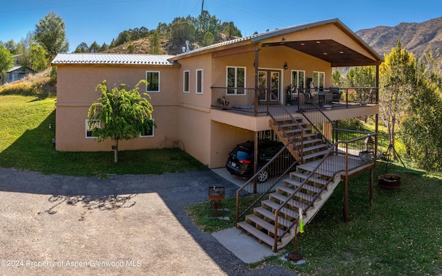 back of property featuring a deck with mountain view, stucco siding, stairway, and a yard