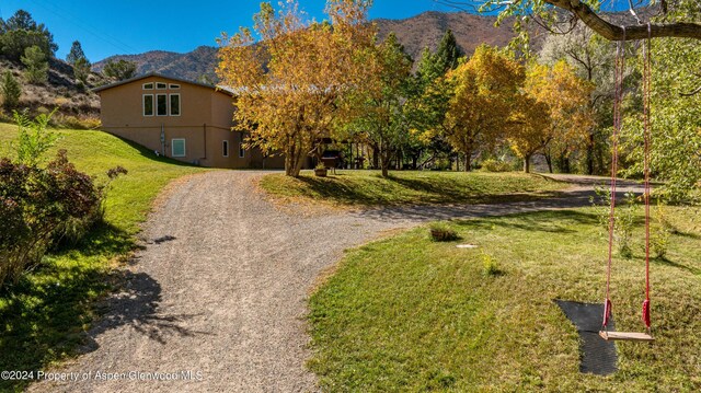 view of front of house with a front lawn, gravel driveway, a mountain view, and stucco siding