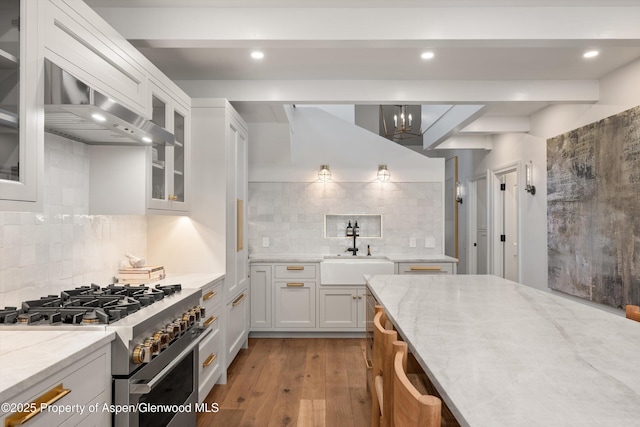 kitchen featuring light stone counters, white cabinetry, a sink, and high end range