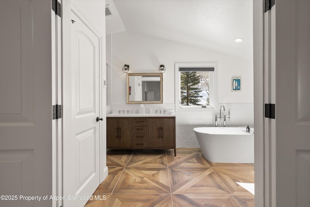 bathroom featuring lofted ceiling, a wainscoted wall, vanity, tile walls, and a freestanding bath