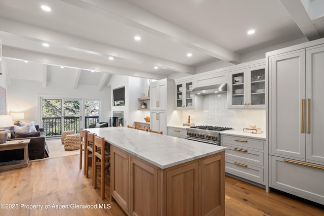 kitchen featuring stainless steel stove, open floor plan, a kitchen island, light stone countertops, and under cabinet range hood