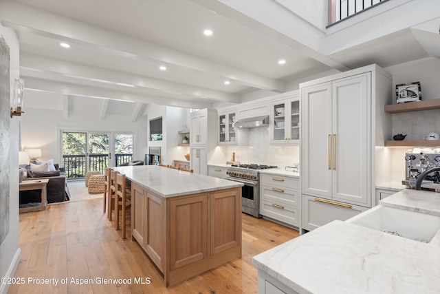 kitchen with open shelves, a kitchen island, a sink, wall chimney range hood, and high end stove