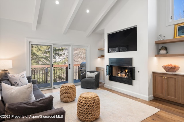 living area featuring beam ceiling, recessed lighting, light wood-style flooring, a glass covered fireplace, and high vaulted ceiling