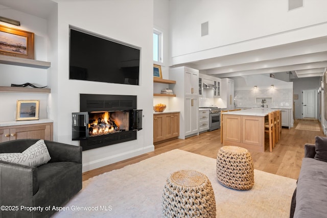 living area featuring a warm lit fireplace, visible vents, light wood-type flooring, and a towering ceiling