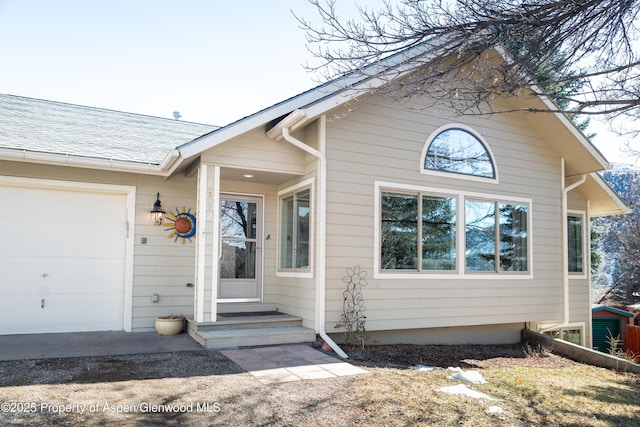 doorway to property featuring a shingled roof and an attached garage