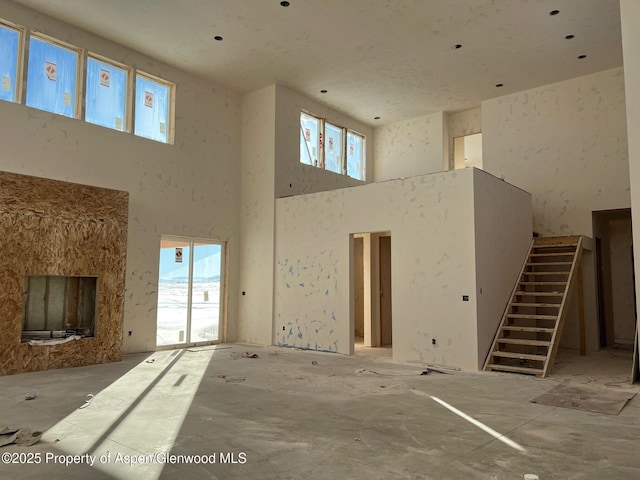 unfurnished living room with a high end fireplace, a healthy amount of sunlight, stairway, and a high ceiling