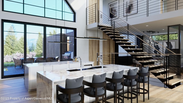 kitchen with light stone counters, a towering ceiling, and light wood-type flooring