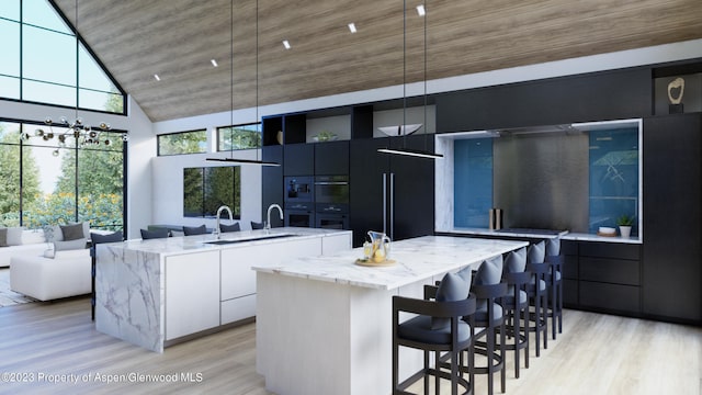 kitchen featuring a kitchen island with sink, white cabinets, black built in fridge, hanging light fixtures, and light stone counters