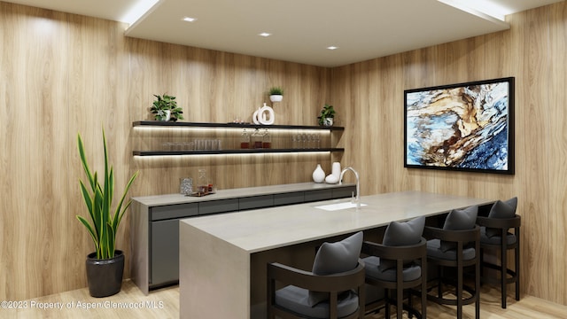 bar with gray cabinetry, sink, and wood walls