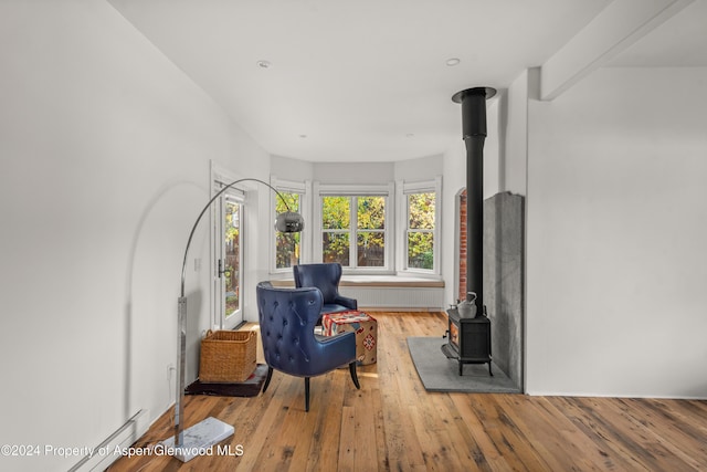 sitting room with a wood stove, light hardwood / wood-style flooring, and a baseboard heating unit