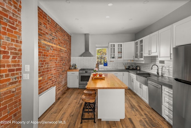 kitchen featuring butcher block counters, white cabinetry, a center island, wall chimney exhaust hood, and stainless steel appliances