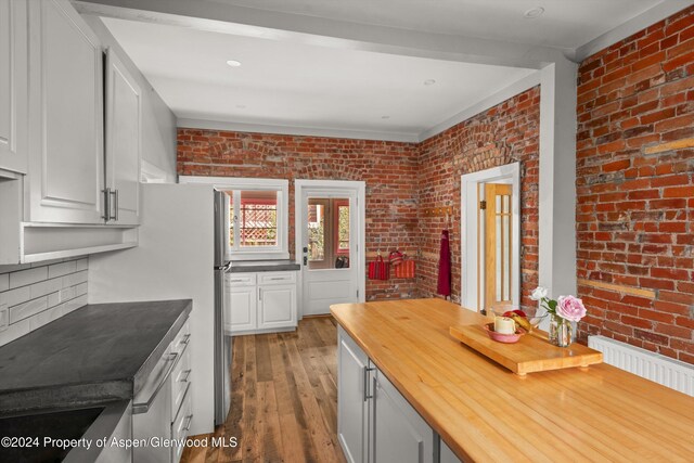 kitchen featuring hardwood / wood-style flooring, white cabinets, and brick wall