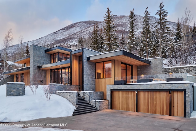 contemporary house featuring a mountain view, a garage, stairs, driveway, and stone siding