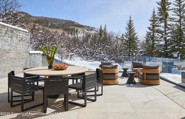 snow covered patio with outdoor dining space and a mountain view