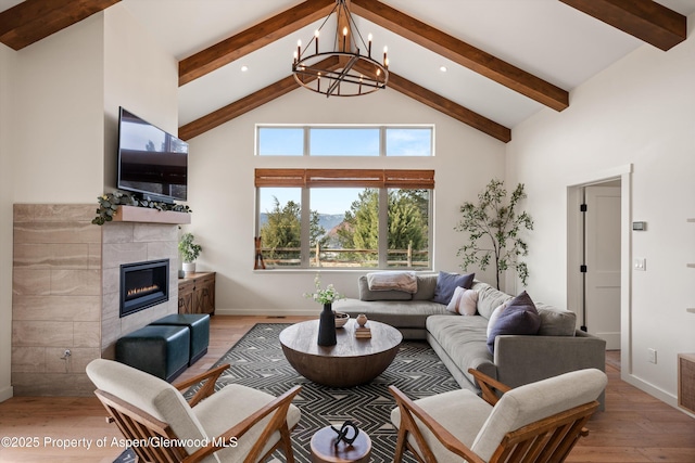 living room featuring high vaulted ceiling, light wood-style floors, a tiled fireplace, beamed ceiling, and a notable chandelier