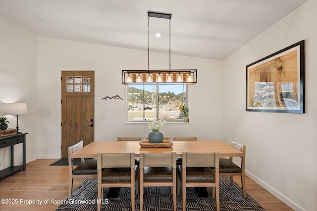 dining area with baseboards, light wood finished floors, and vaulted ceiling