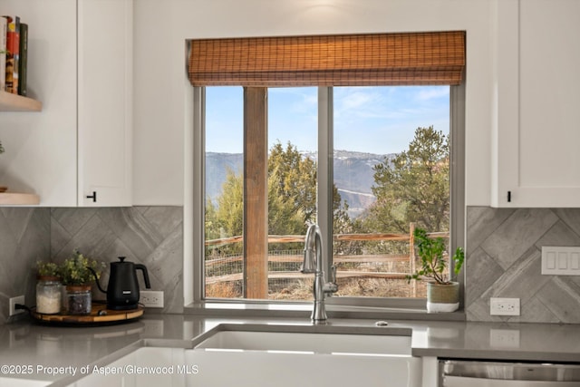 interior space with backsplash, stainless steel dishwasher, a sink, and white cabinetry