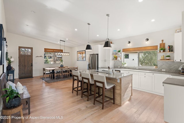 kitchen featuring a breakfast bar area, light wood finished floors, open shelves, vaulted ceiling, and stainless steel refrigerator with ice dispenser