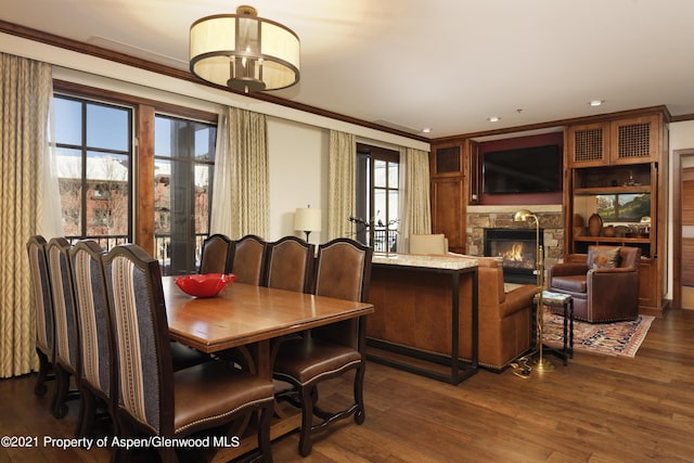 dining space with dark hardwood / wood-style floors, a stone fireplace, ornamental molding, and a wealth of natural light