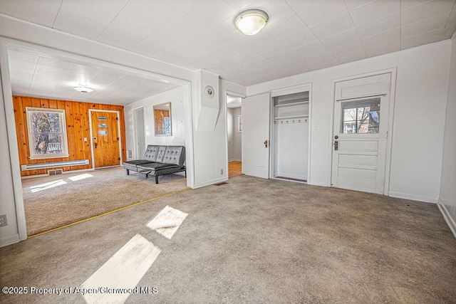 foyer entrance featuring wood walls, carpet flooring, and baseboards