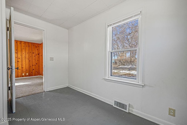 empty room featuring ornamental molding, visible vents, wooden walls, and baseboards