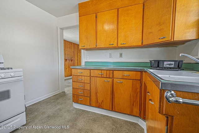 kitchen featuring brown cabinets, a sink, gas range gas stove, and baseboards