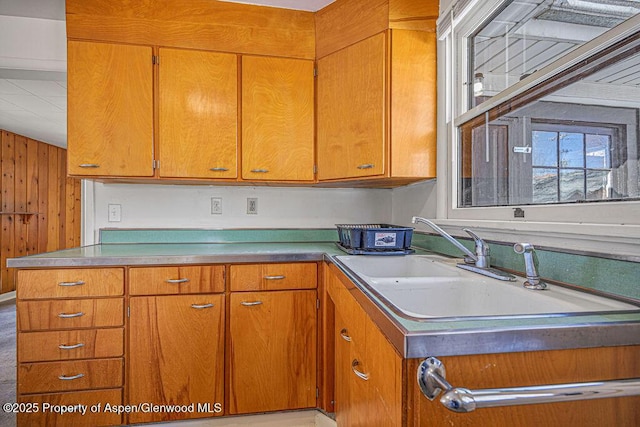 kitchen with brown cabinetry, light countertops, a sink, and wooden walls