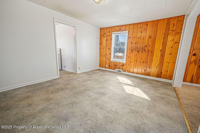 spare room with carpet floors, baseboards, wooden walls, and visible vents