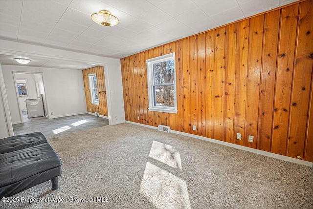 living area with carpet floors, wooden walls, visible vents, and baseboards