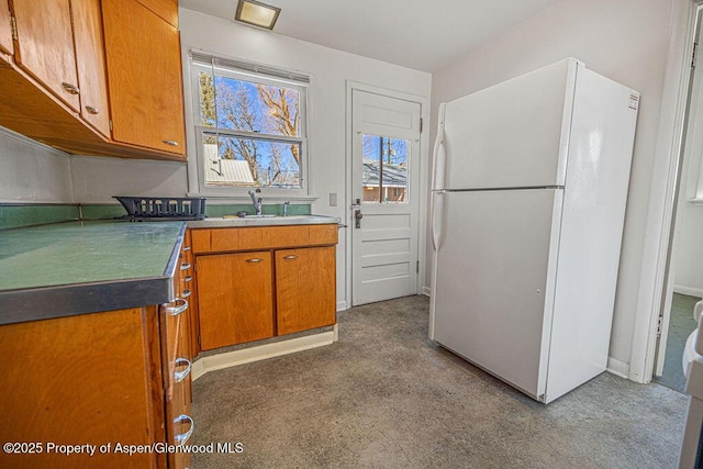 kitchen featuring freestanding refrigerator, brown cabinets, and a sink