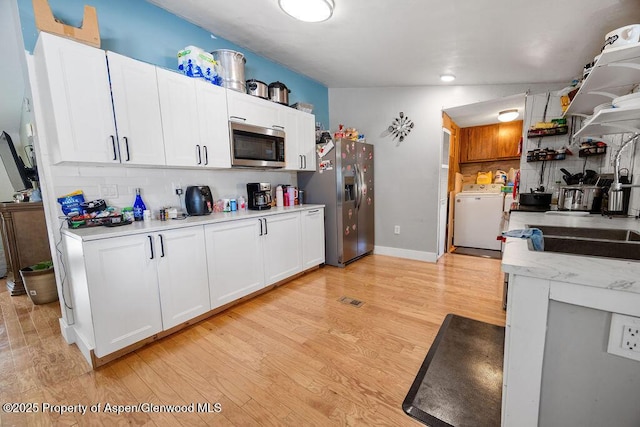 kitchen with washer / clothes dryer, stainless steel appliances, white cabinets, and light wood-type flooring